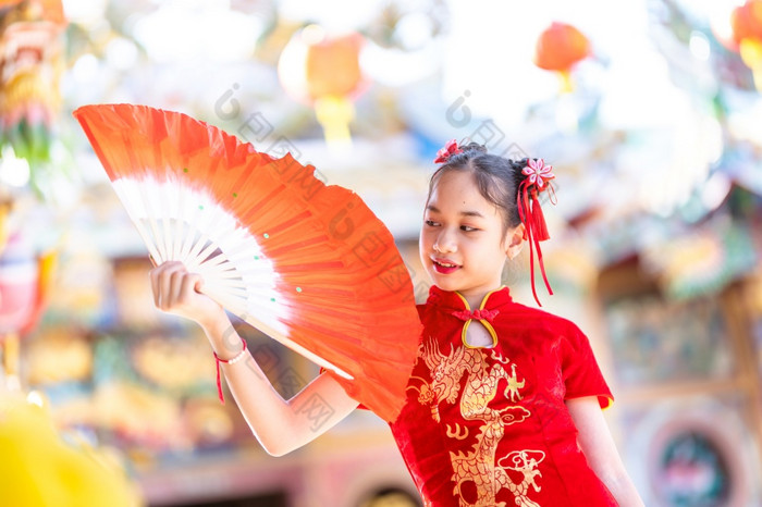 肖像美丽的微笑可爱的小亚洲女孩穿红色的传统的中国人旗袍装饰和持有范宁为中国人新一年节日中国人神社