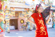 肖像美丽的微笑可爱的小亚洲女孩穿红色的传统的中国人旗袍装饰和持有范宁为中国人新一年节日中国人神社