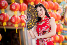 肖像美丽的微笑亚洲年轻的女人穿红色的传统的中国人旗袍装饰和持有中国人范宁为中国人新一年节日中国人神社泰国