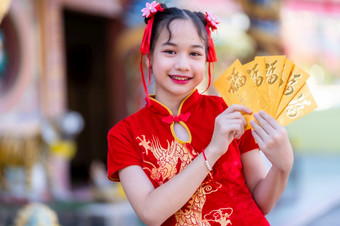 肖像可爱的小亚洲女孩穿红色的传统的中国人旗袍装饰持有黄色的信封与的中国人文本祝福写好运气为中国人新一年节日