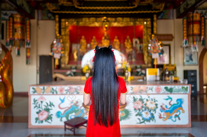 美丽的可爱的小亚洲年轻的女人穿红色的传统的中国人旗袍装饰站为祈祷佛雕像为中国人新一年节日中国人神社泰国