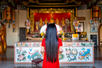 美丽的可爱的小亚洲年轻的女人穿红色的传统的中国人旗袍装饰站为祈祷佛雕像为中国人新一年节日中国人神社泰国