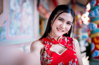 肖像美丽的微笑亚洲年轻的女人穿红色的传统的中国人旗袍装饰采取自拍与智能手机为中国人新一年节日中国人神社