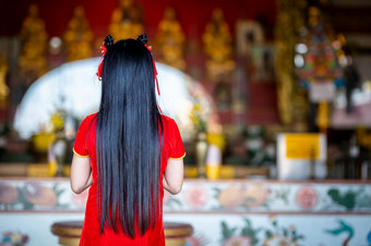 美丽的可爱的小亚洲年轻的女人穿红色的传统的中国人旗袍装饰站为祈祷佛雕像为中国人新一年节日中国人神社泰国