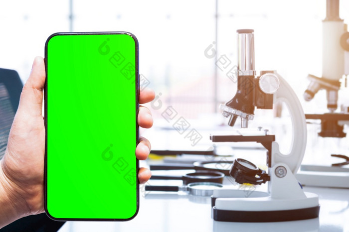 特写镜头女使用绿色屏幕智能手机模糊图片与显微镜和测试管与实验室玻璃器皿实验室背景研究和科学概念