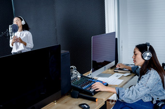 女技术员的电脑<strong>监控</strong>为记录前面控制桌子上<strong>设备</strong>为年轻的亚洲女人歌手穿耳机记录首歌前面麦克风专业工作室
