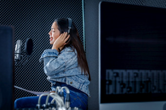 快乐漂亮的微笑年轻的亚洲女人歌手穿耳机记录首歌前面麦克风的电脑监控软件为记录和编辑听起来专业工作室