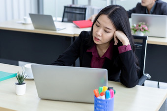 心烦意乱深思熟虑的年轻的亚洲业务女人压力的工作场所工作与移动PC电脑办公室工作人员是不快乐与工作的同事们<strong>后面</strong>的办公室