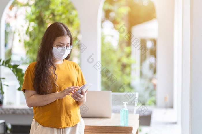 自由人业务女穿保护面具休闲和写作消息智能手机工作与移动PC电脑工作从首页概念预防的传播新冠病毒病毒