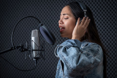 快乐快乐的漂亮的微笑肖像年轻的亚洲女人歌手穿耳机记录首歌前面麦克风专业工作室