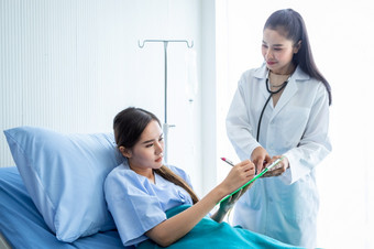 亚洲年轻的女病人签名为同意形式床上女医生治疗建议与积极的情绪的房间医院背景
