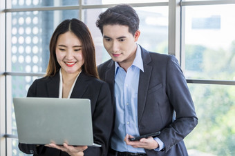 年轻的亚洲女商人和商人合作伙伴而工作在一起与移动PC电脑和业务男人。持有平板电脑办公室背景工作夫妇