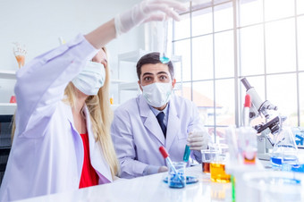 两个科学家们穿卫生保护面具是工作持有看测试管与样本化学实验室科学家是做调查实验室分析背景