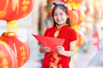 亚洲快乐小女孩穿红色的传统的中国人旗袍装饰持有红色的信封手和灯笼与的中国人文本祝福写《财富》杂志祝福为中国人