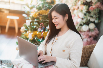 肖像自由业务微笑年轻的亚洲女人持有杯咖啡在线工作与移动PC电脑首页的生活房间在室内装饰在圣诞节x-mas和新一年假期