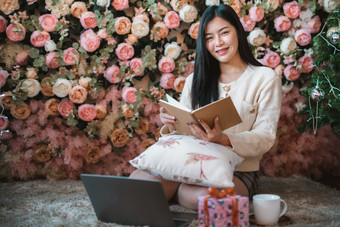 肖像可爱的美丽的积极的微笑年轻的亚洲女人持有读书与移动PC电脑首页的生活房间在室内装饰在圣诞节x-mas和新一年假期
