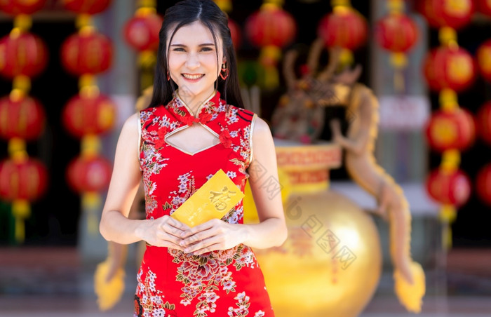 肖像亚洲年轻的女人穿红色的旗袍衣服传统的装饰持有黄色的信封与的中国人文本祝福写好运气为中国人新一年节日