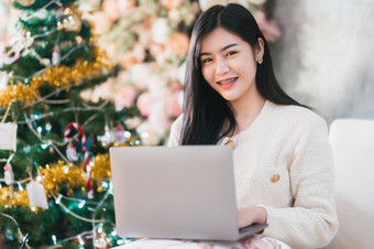 肖像自由业务微笑年轻的亚洲女人持有杯咖啡在线工作与移动PC电脑首页的生活房间在室内装饰在圣诞节x-mas和新一年假期
