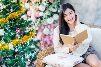 肖像可爱的美丽的积极的微笑年轻的亚洲女人持有读书首页的生活房间在室内装饰在圣诞节x-mas和新一年假期