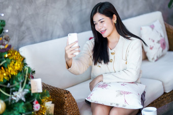 肖像可爱的美丽的积极的微笑年轻的亚洲女人使用智能手机视频调用自拍首页的生活房间在室内<strong>装饰</strong>在圣诞节x-mas和新一年假期