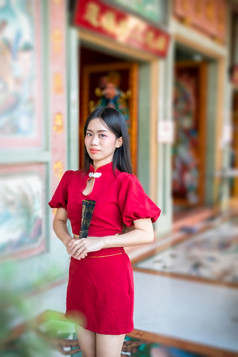 肖像美丽的微笑亚洲年轻的女人穿红色的传统的中国人旗袍装饰和持有中国人范宁为中国人新一年节日中国人神社泰国