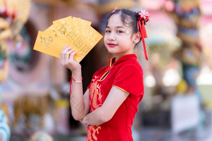 肖像可爱的小亚洲女孩穿红色的传统的中国人旗袍装饰持有黄色的信封与的中国人文本祝福写好运气为中国人新一年节日