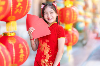 亚洲快乐小女孩穿红色的传统的中国人旗袍装饰持有红色的信封手和灯笼与的中国人文本祝福写《财富》杂志祝福为中国人