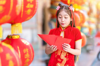 亚洲快乐小女孩穿红色的传统的中国人旗袍装饰持有红色的信封手和灯笼与的中国人文本祝福写《财富》杂志祝福为中国人