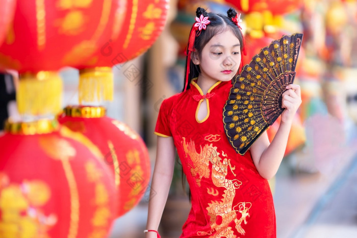 小亚洲女孩穿红色的传统的中国人旗袍和持有范宁和灯笼与的中国人字母祝福写《财富》杂志祝福赞美装饰为新一年