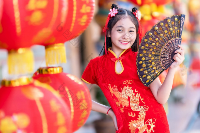 小亚洲女孩穿红色的传统的中国人旗袍和持有范宁和灯笼与的中国人字母祝福写《财富》杂志祝福赞美装饰为新一年