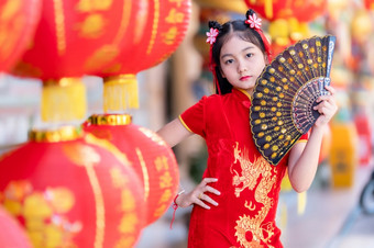 小亚洲女孩穿红色的传统的中国人旗袍和持有范宁和灯笼与的中国人字母祝福写《财富》杂志祝福赞美装饰为新一年