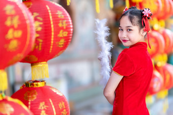 小亚洲女孩穿红色的传统的中国人旗袍和持有范宁和灯笼与的中国人字母祝福写《财富》杂志祝福赞美装饰为新一年