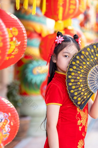 小亚洲女孩穿红色的传统的中国人旗袍和持有范宁和灯笼与的中国人字母祝福写《财富》杂志祝福赞美装饰为新一年