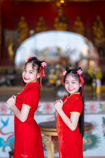 肖像美丽的微笑可爱的小亚洲两个女孩穿红色的传统的中国人旗袍装饰为中国人新一年节日中国人神社