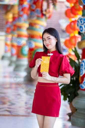 肖像亚洲年轻的女人穿红色的传统的中国人旗袍装饰持有黄色的报业信封与的中国人文本祝福写好运气为快乐中国人新一年