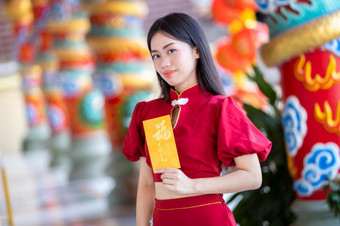 肖像亚洲年轻的女人穿红色的传统的中国人旗袍装饰持有黄色的报业信封与的中国人文本祝福写好运气为快乐中国人新一年