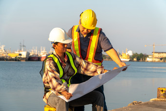 两个工程师站在穿安全头盔站的码头和持有的蓝图和咨询的计划的建设概念非常<strong>高效</strong>。建设管理
