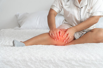 超重女人坐着的床上和捕捉的膝盖因为的疼痛引起的超重问题概念健康问题肥胖人