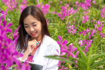 快乐研究员植物研究兰花穿白色帽和她的手持有笔和笔记本为采取笔记为研究