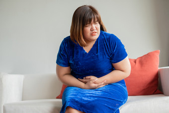 超大的亚洲女人坐着沙发生活房间她的心烦意乱和不开心和持有手胃痛苦从腹部疼痛概念期抽筋胃炎和健康哪