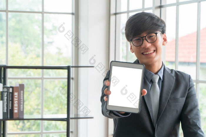 年轻的亚洲商人穿西装持有和显示前面一边视图白色空白屏幕平板电脑模型概念专业介绍你自己空白屏幕为文本和内容广告