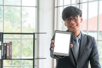 年轻的亚洲商人穿西装持有和显示前面一边视图白色空白屏幕平板电脑模型概念专业介绍你自己空白屏幕为文本和内容广告