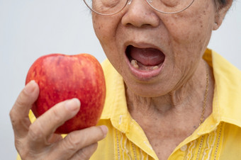 老女人穿眼镜和没有牙齿尝试吃红色的苹果概念牙科健康问题上了年纪的病人医疗和医疗保健概念