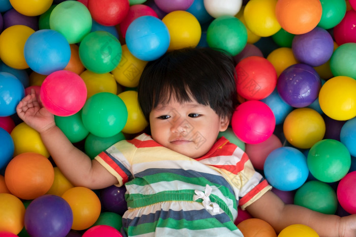 快乐亚洲女孩一个和一半年岁的玩小色彩斑斓的球池球的概念玩的最好的学习为孩子们