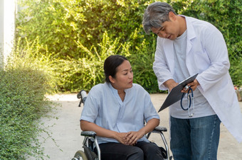 的医生持有的剪贴板和解释健康问题和的效果治疗为病人坐着轮椅而走的花园概念医疗保健和医疗服务
