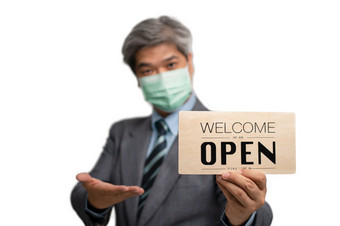 亚洲商人穿医疗面具的孤立的背景和持有欢迎是开放标志的概念企业和商店有开放后的情况开始放松