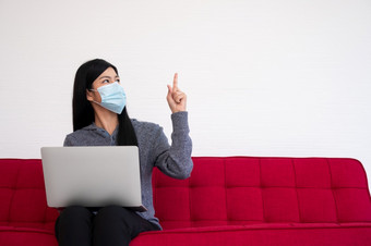 亚洲女人穿脸面具和使用移动PC的沙发为工作从首页和指出的前<strong>新生活方式</strong>正常的在检疫概念保持首页