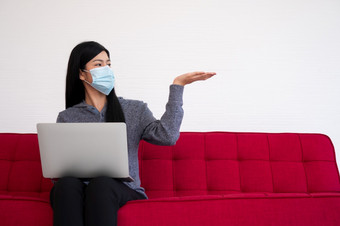 亚洲女人穿脸面具和使用移动PC的沙发为工作从首页新生活方式正常的在检疫概念保持首页