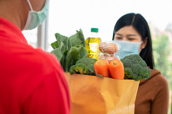 亚洲女人穿脸面具和皮卡购物袋新鲜的食物蔬菜和<strong>水果</strong>从交付男人。从<strong>超市</strong>概念表达杂货店服务和新生活方式