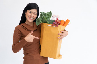 快乐亚洲女人微笑和点的手指纸袋和携带购物袋后的快递从杂货店来了交付首页概念超市交付为新生活方式